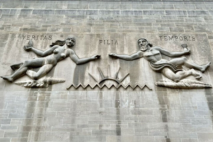 A carving with the Latin words "veritas," "filia," and "temporis" on the exterior of a limestone building.